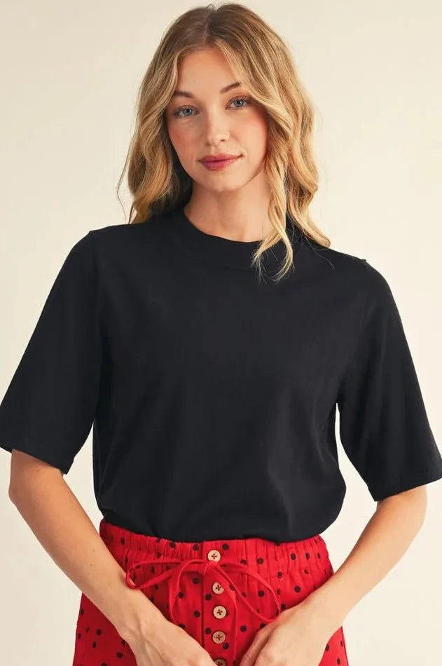 Woman wearing a black top and red polka dot pants on a beige background