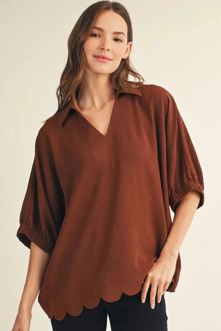 Woman wearing a brown scalloped blouse against a beige background
