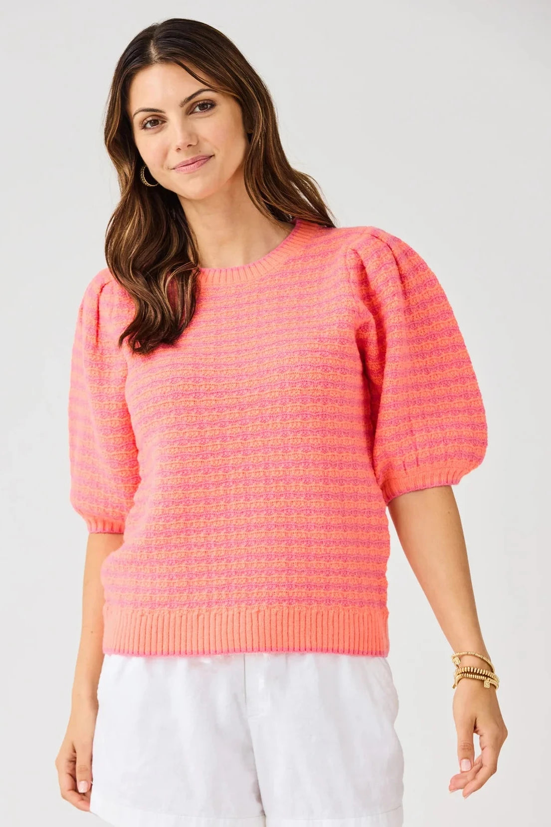 Woman wearing a pink sweater with puff sleeves on a plain background